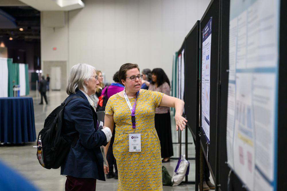 A researcher presents their poster to another conference attendee